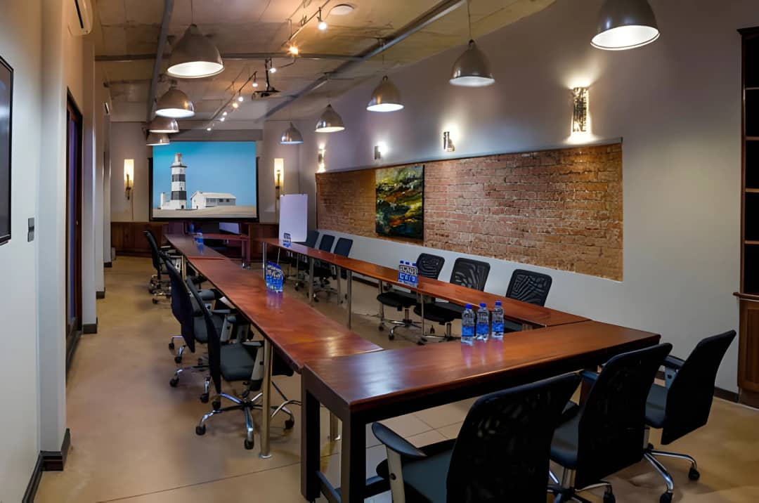 Conference room with U-shaped table, projector screen, exposed brick wall.