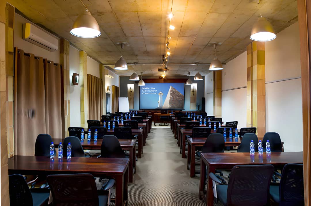 Conference room set with desks, chairs, water bottles, and projector screen.