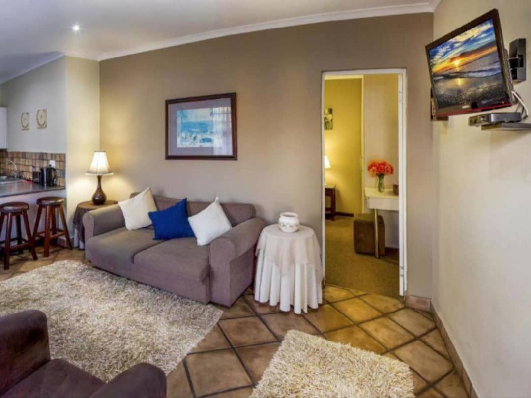 Open-plan lounge with sofa, mounted TV, kitchenette, and tiled floor.
