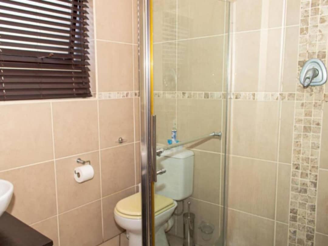 Tiled bathroom with glass shower door, toilet, and wooden blinds.